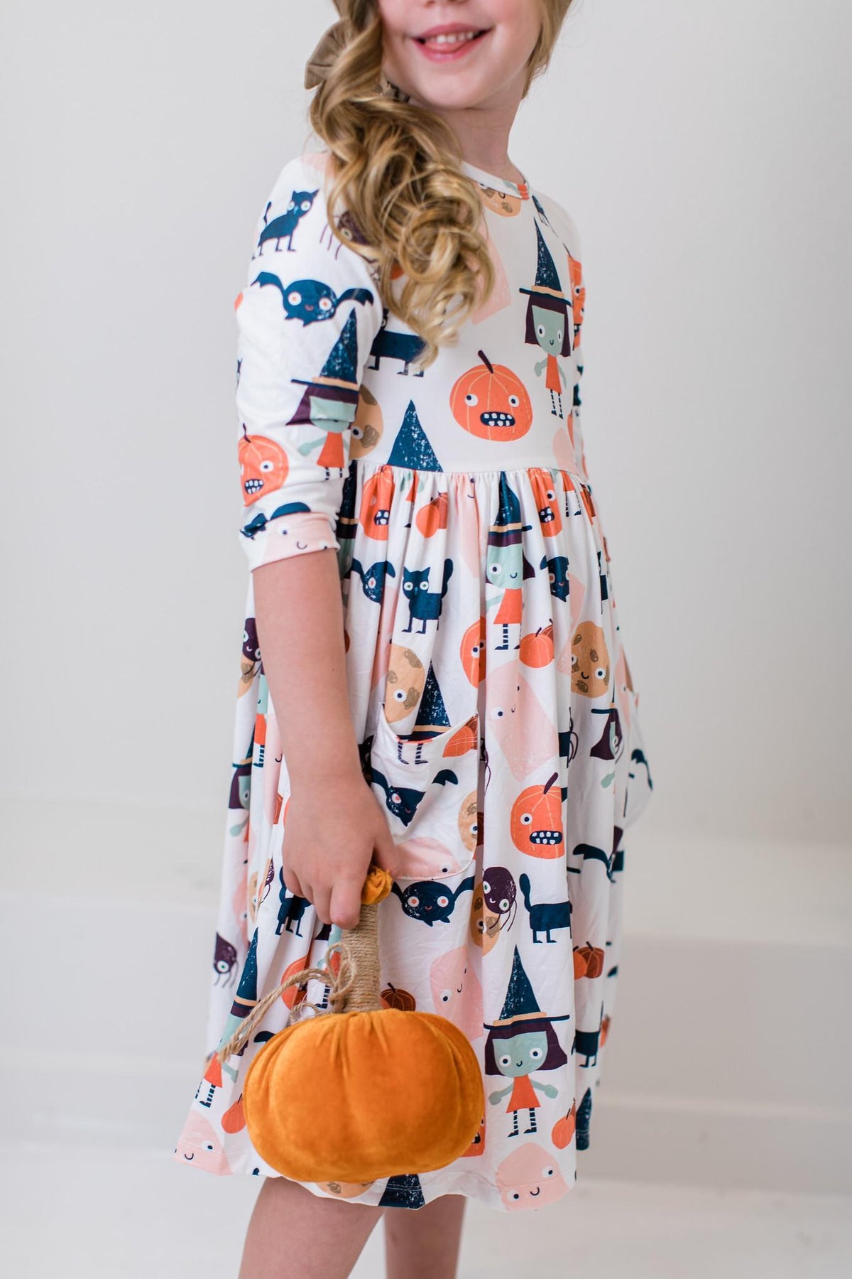 Girl holding a small jack-o'-lantern prop while wearing the Boo Crew twirl dress.