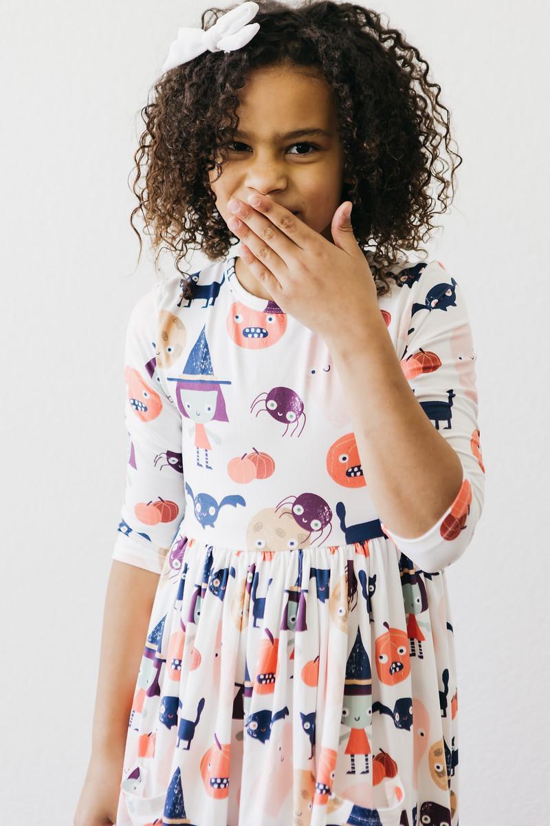 Girl smiling with a hand near her face, wearing the Boo Crew twirl dress.