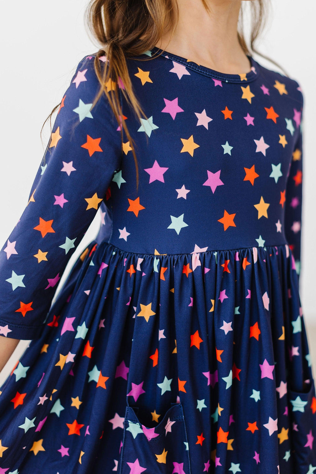 Close-up of the Halloween Stars twirl dress showing the neckline with a small button, a three-quarter sleeve, the gathered waist seam, a patch pocket and the multicolour star print on navy fabric.