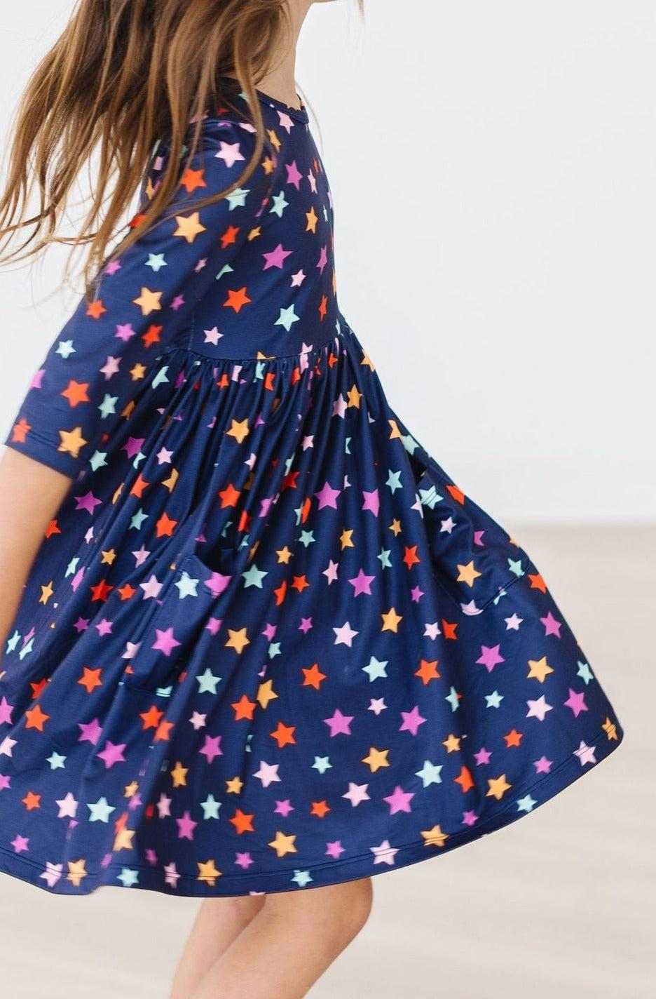 Close-up of the Halloween Stars dress skirt flaring mid-twirl, showing the patch pocket, gathered pleats and the multicolour star print on navy; the wearer's head is partly out of frame.