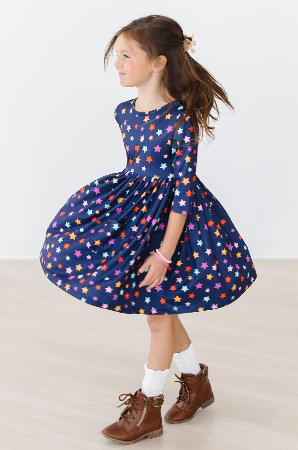 Side view of the Halloween Stars twirl dress with the skirt flared, showing the three-quarter sleeve, fitted bodice and multicolour star print on navy, worn with white socks and brown lace-up boots.