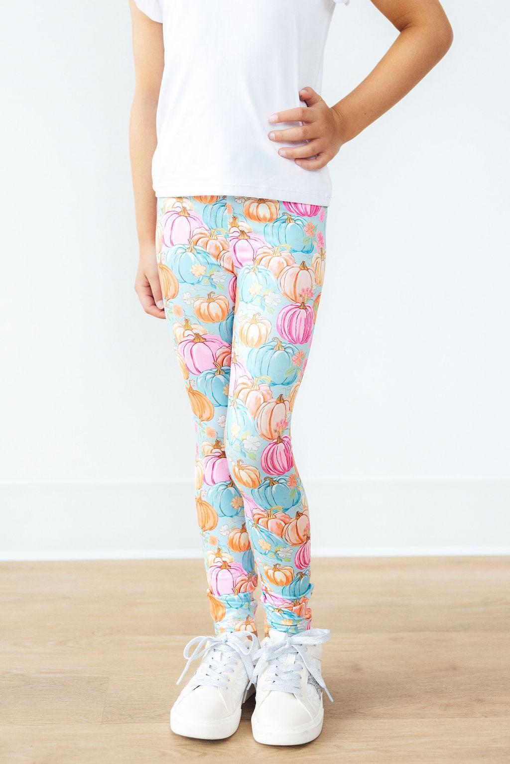 Girl photographed from the waist down wearing the Preppy Pumpkins leggings with a white tee and white sneakers on a light wood floor.