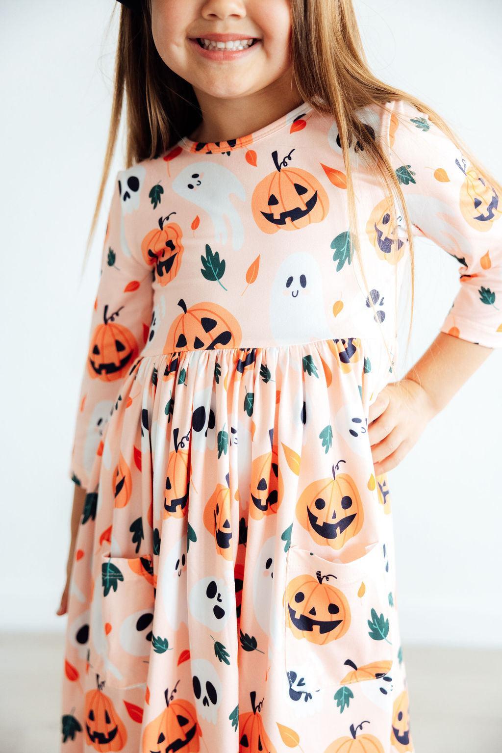 Close-up of the Pumpkin Peekaboo print: orange jack-o'-lanterns, white ghosts, black bats and fall leaves on a soft peach ground.