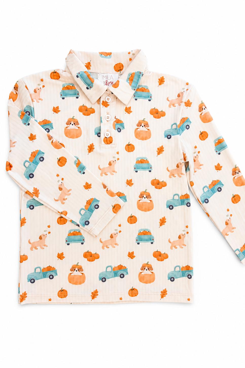 Flat lay of the Mila & Rose Pumpkin Spice Pups boys' long-sleeve polo, showing puppies in blue pickup trucks loaded with pumpkins, plus leaves and acorns on a cream ground.