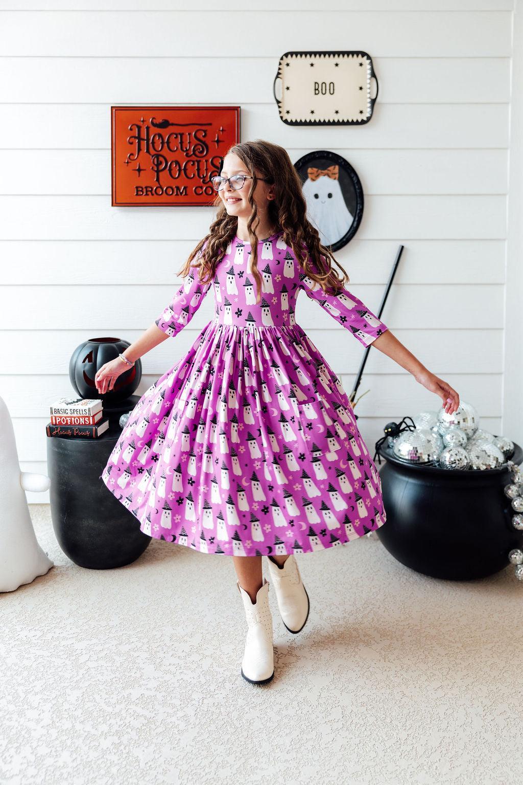 Girl twirling in the Witches Boo twirl dress in front of a Halloween wall sign.