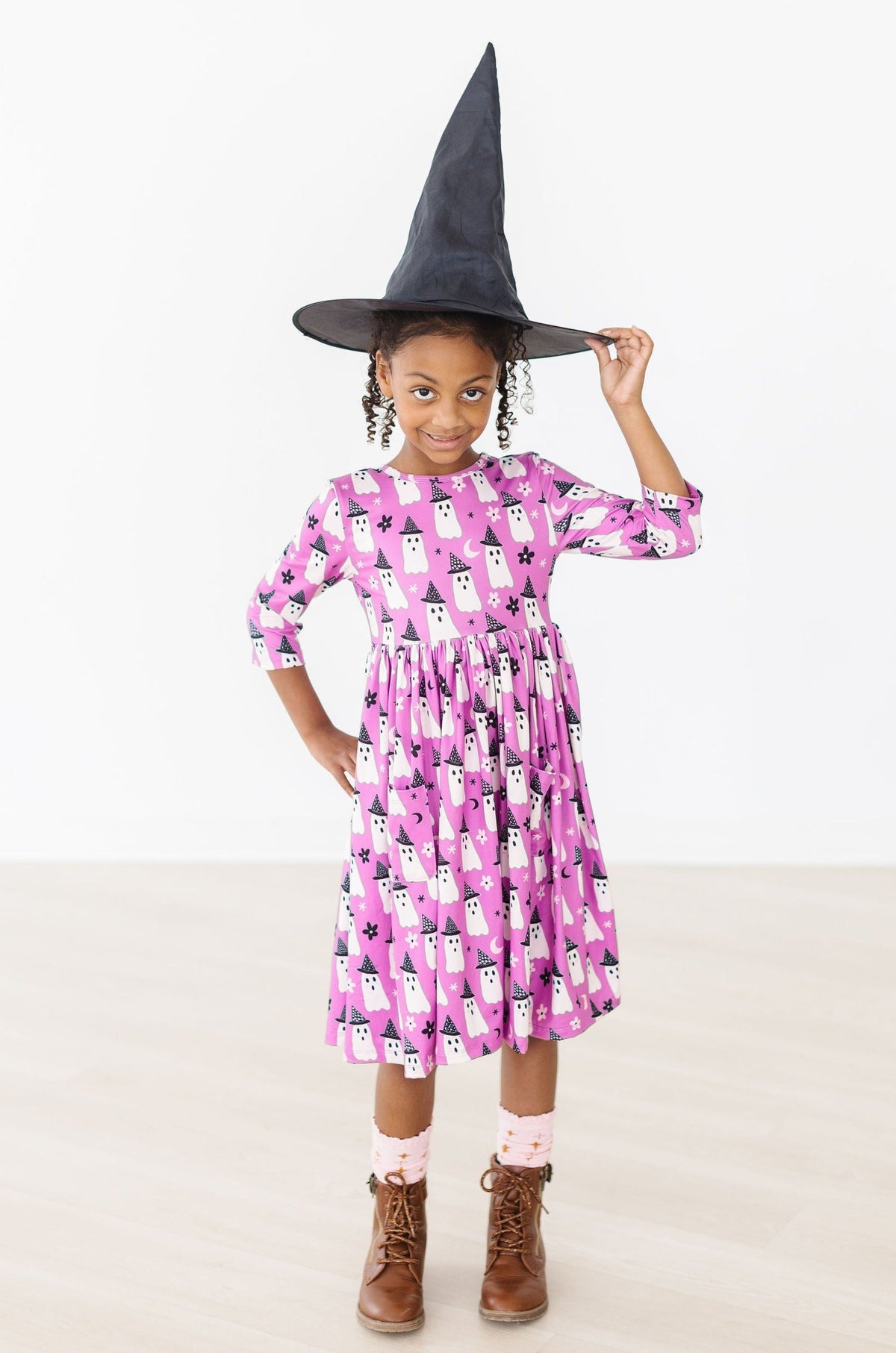 Girl in a black witch hat holding the skirt of the Witches Boo twirl dress out to the side.