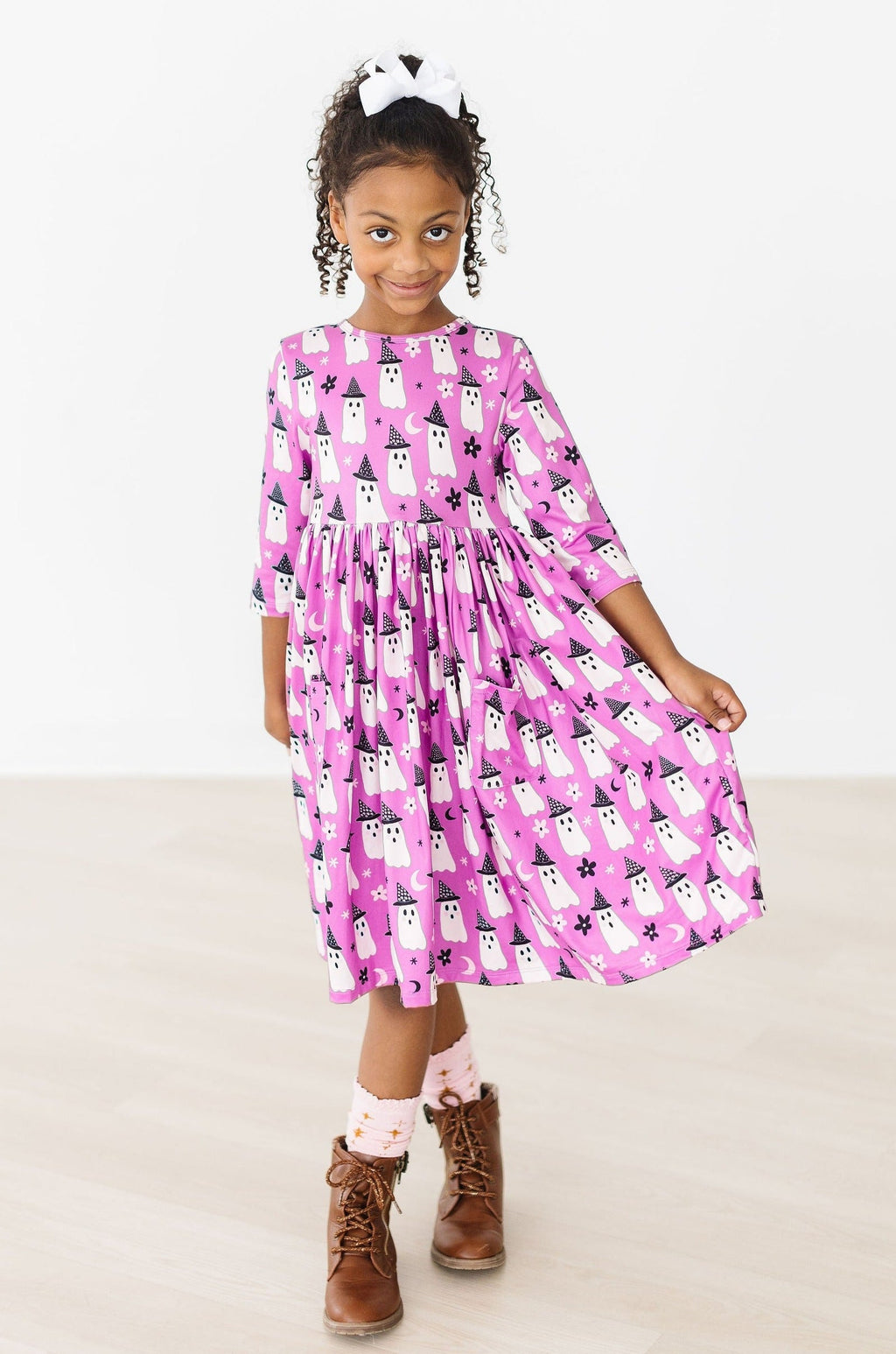 Girl standing with her hands at her sides in the Witches Boo twirl dress and brown boots, full length.