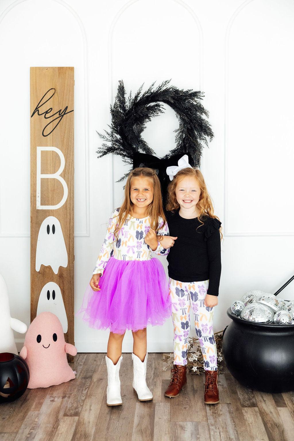 Two girls in a Halloween porch display, one wearing the Tied with a Boo leggings.