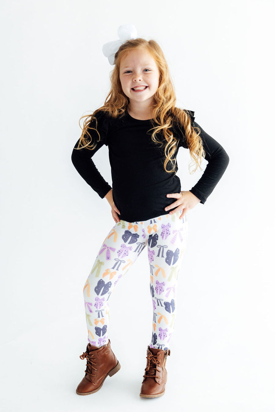 Girl with her hands on her hips wearing the Tied with a Boo leggings and a black top, full length.